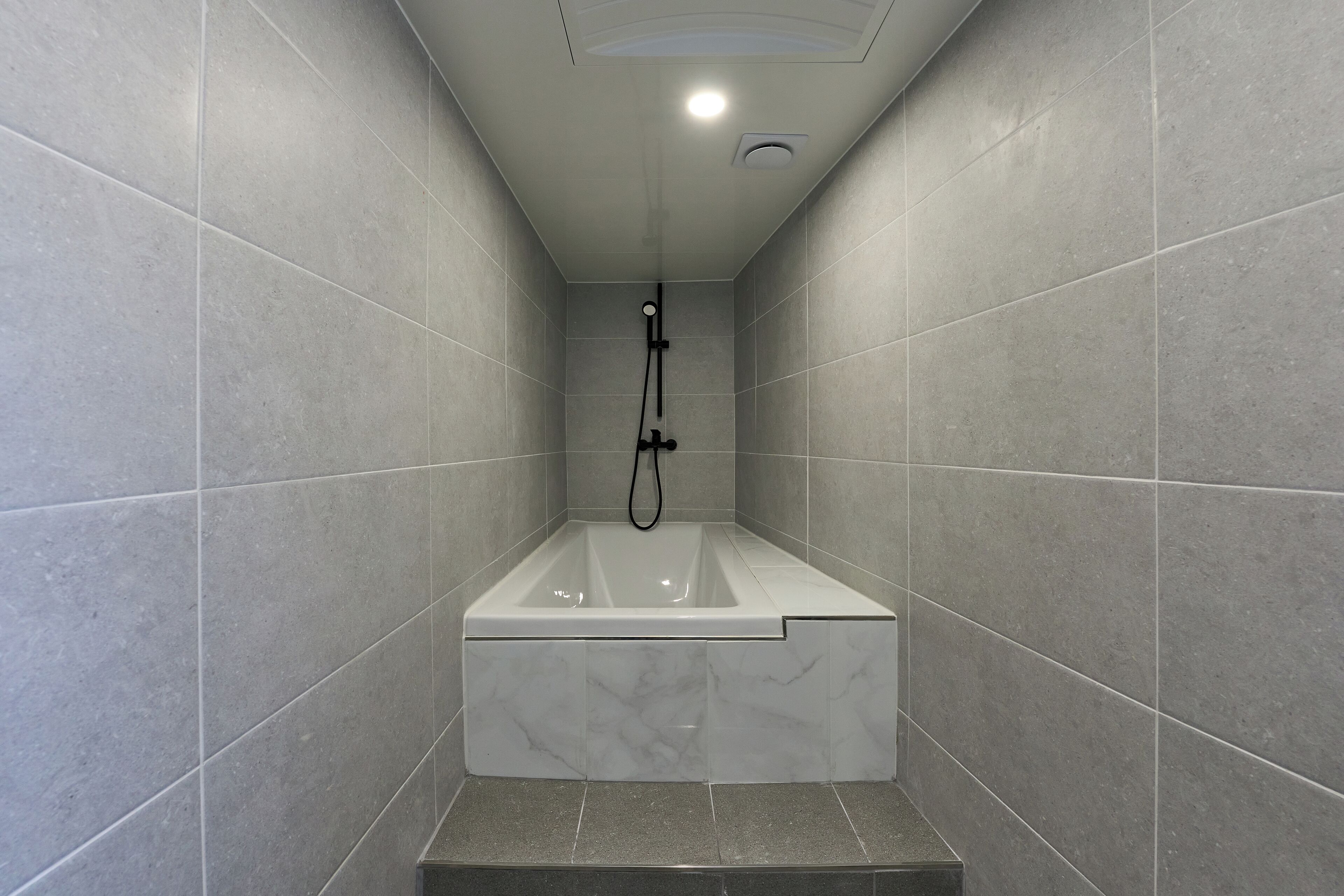 Ein modernes Badezimmer mit einer rechteckigen Badewanne, gefliesten Wänden und einer Deckenleuchte.
