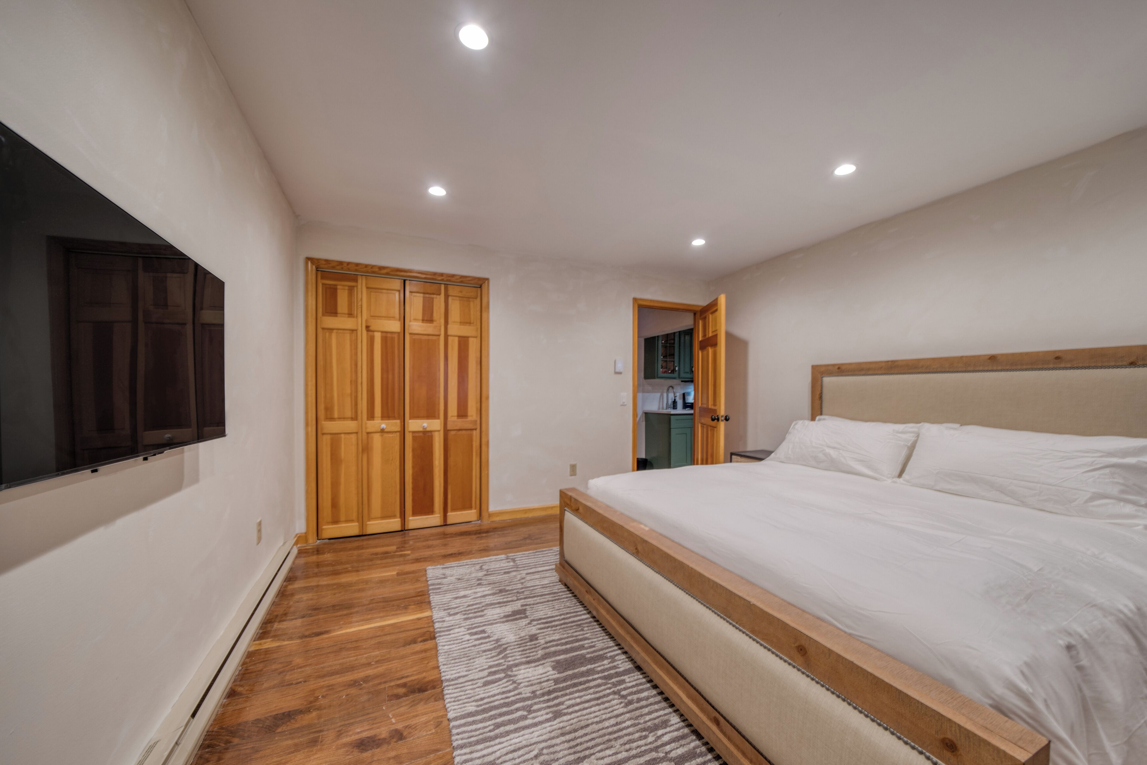 Een slaapkamer met een groot bed, een houten garderobe en een televisie aan de muur.