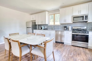 Una cocina moderna con armarios blancos, electrodomésticos de acero inoxidable, una mesa de comedor de mármol y sillas de madera.