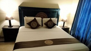 A hotel room with a large bed, two nightstands, and a headboard with a decorative pattern. - Infinity Hotel  (Lahore)