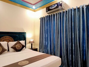A hotel room with a bed, a nightstand with a lamp, and a ceiling-mounted air conditioner. - Infinity Hotel  (Lahore)