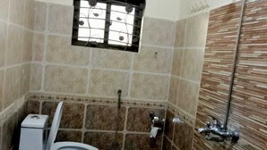 A bathroom with a toilet, shower, and a window with a fan. - Infinity Hotel  (Lahore)
