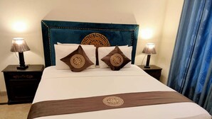 A bed with a decorative headboard, two bedside tables with lamps, and a blue curtain. - Infinity Hotel  (Lahore)