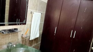 A bathroom with a glass sink, dark wooden wardrobe, and a mirror above the sink. - Infinity Hotel  (Lahore)