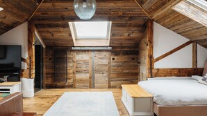 Un dormitorio con techo de madera, tragaluz, cama, mesita de noche y televisor.