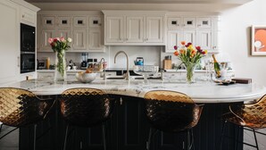 Una cocina moderna con armarios blancos, una isla de mármol y sillas negras.