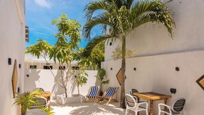 A patio with a wooden table and chairs, surrounded by palm trees and potted plants. - Dhoani Maldives Guesthouse (Kendhoo)