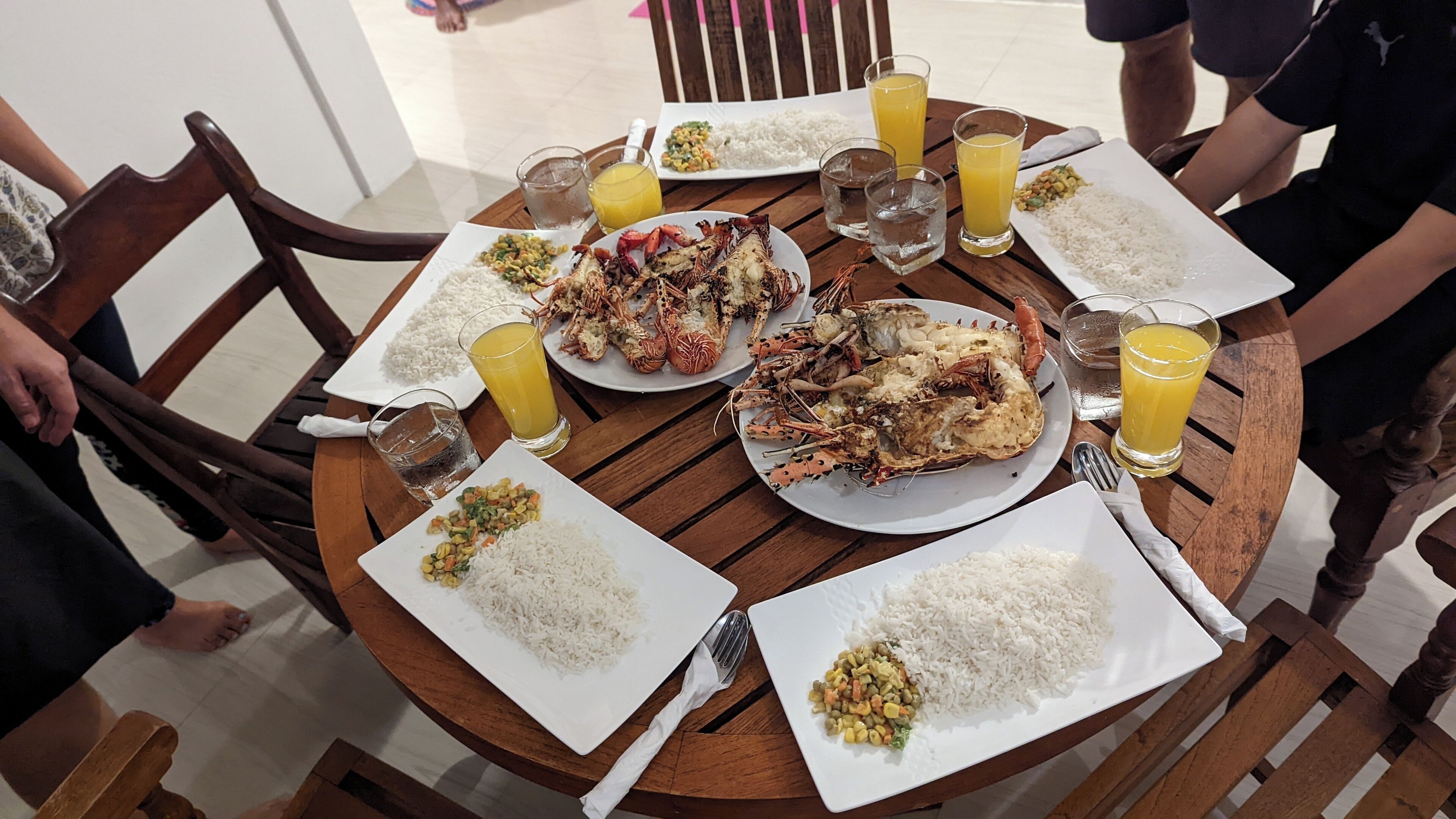 A round wooden table with plates of rice and lobster, glasses of orange juice, and a white plate with a vegetable dish.