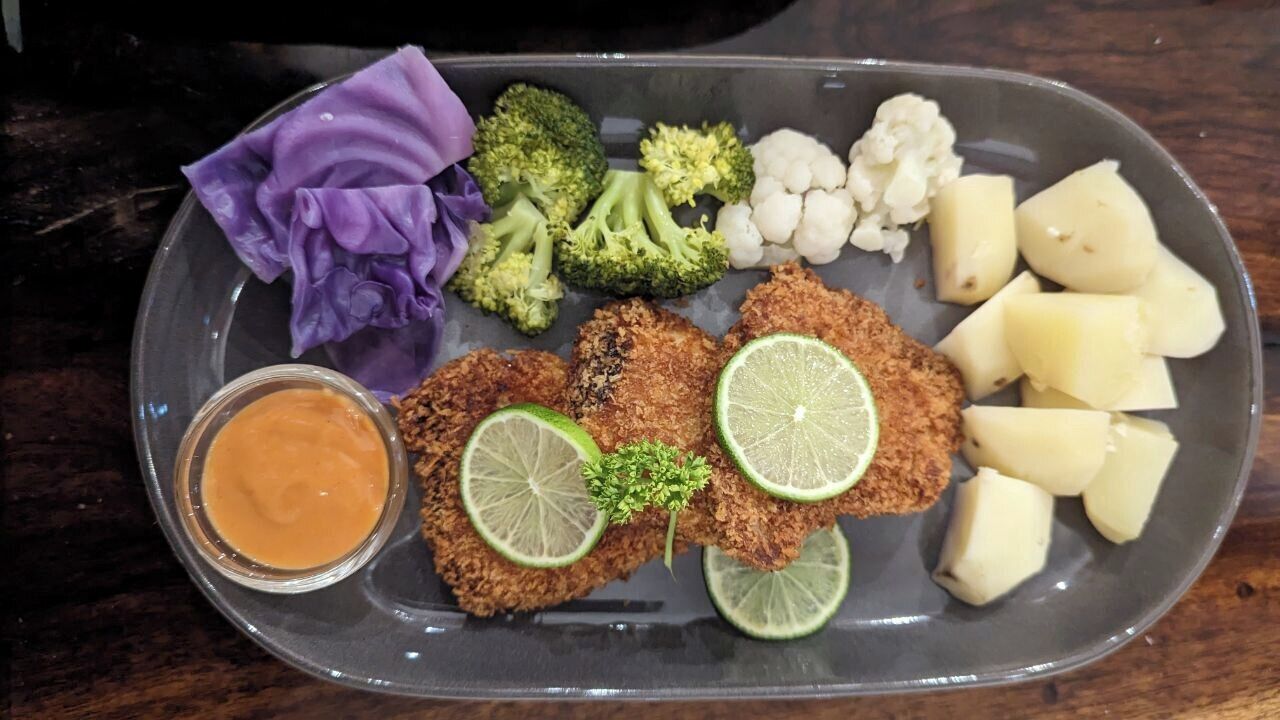 A meal tray with breaded cutlets, potatoes, cauliflower, broccoli, purple cabbage, and a side of sauce.