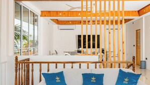 A modern living room with a sofa, a dining area, and a wooden staircase. - Dhoani Maldives Guesthouse (Kendhoo)