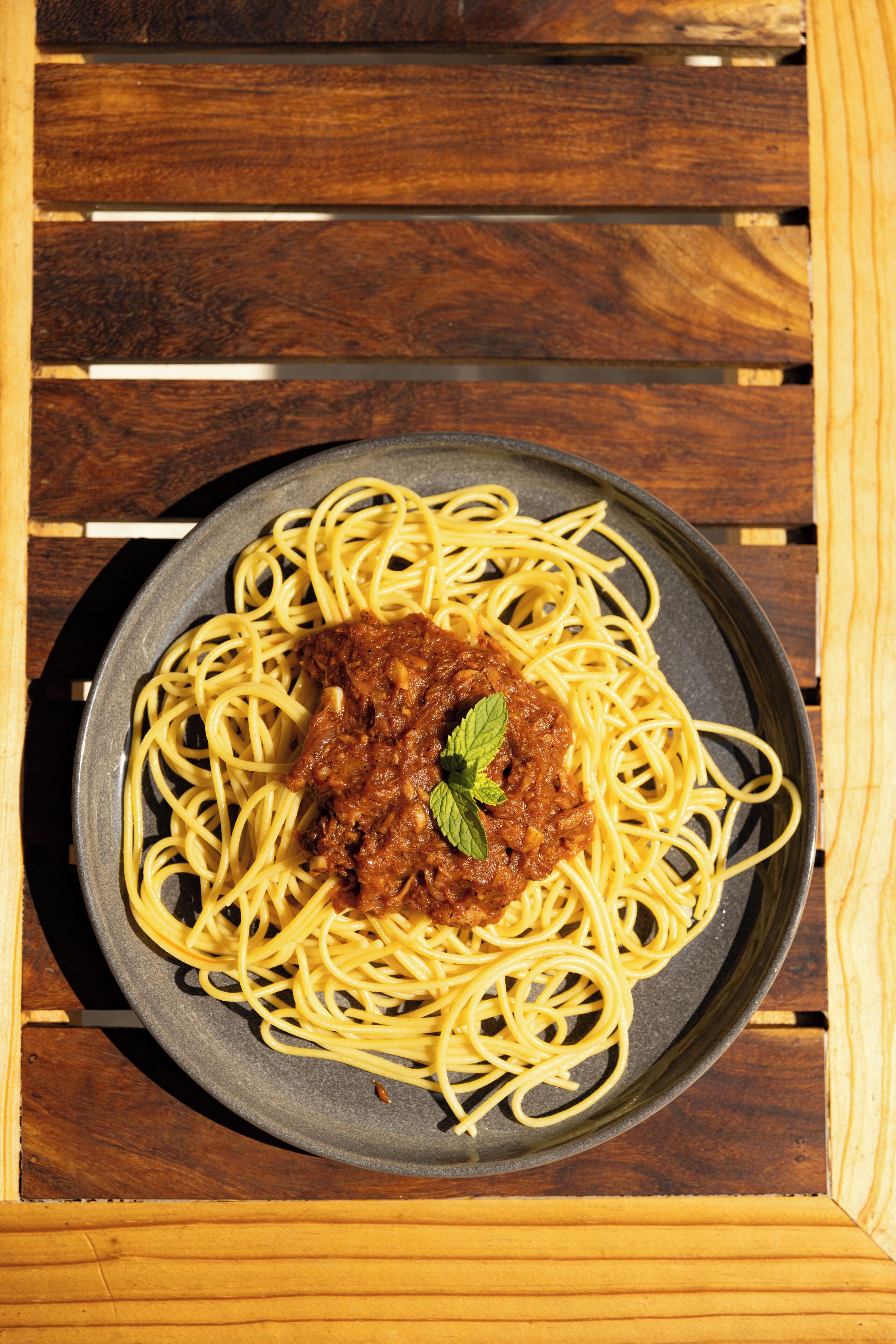 Un piatto di spaghetti con ragù di carne e una foglia di menta come guarnizione, su un piatto scuro.