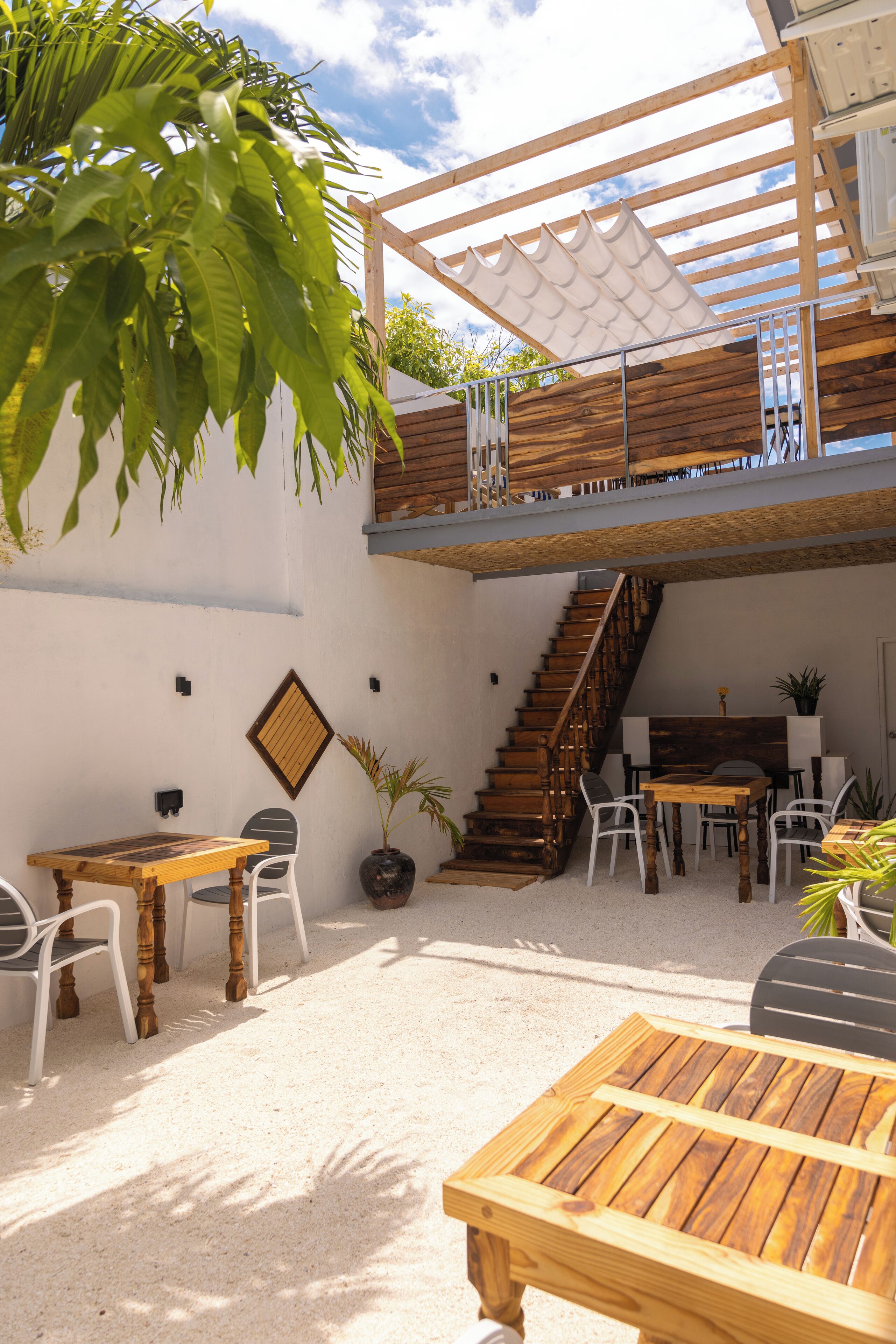 Une terrasse extérieure avec des meubles en bois, un escalier et un mur blanc.