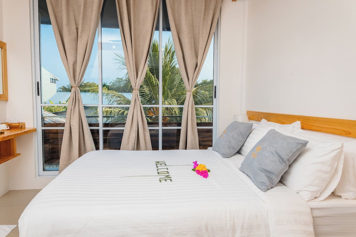 A hotel room with a large bed, a window with curtains, a wooden headboard, and a welcome sign on the bed.