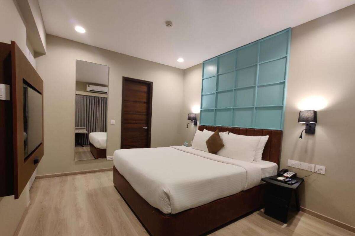 A modern hotel room with a large bed, a nightstand, a wall-mounted TV, and a mirror.