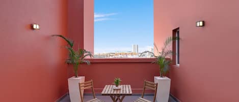 A balcony with two wooden chairs and a small table, potted plants, and a view of the cityscape.