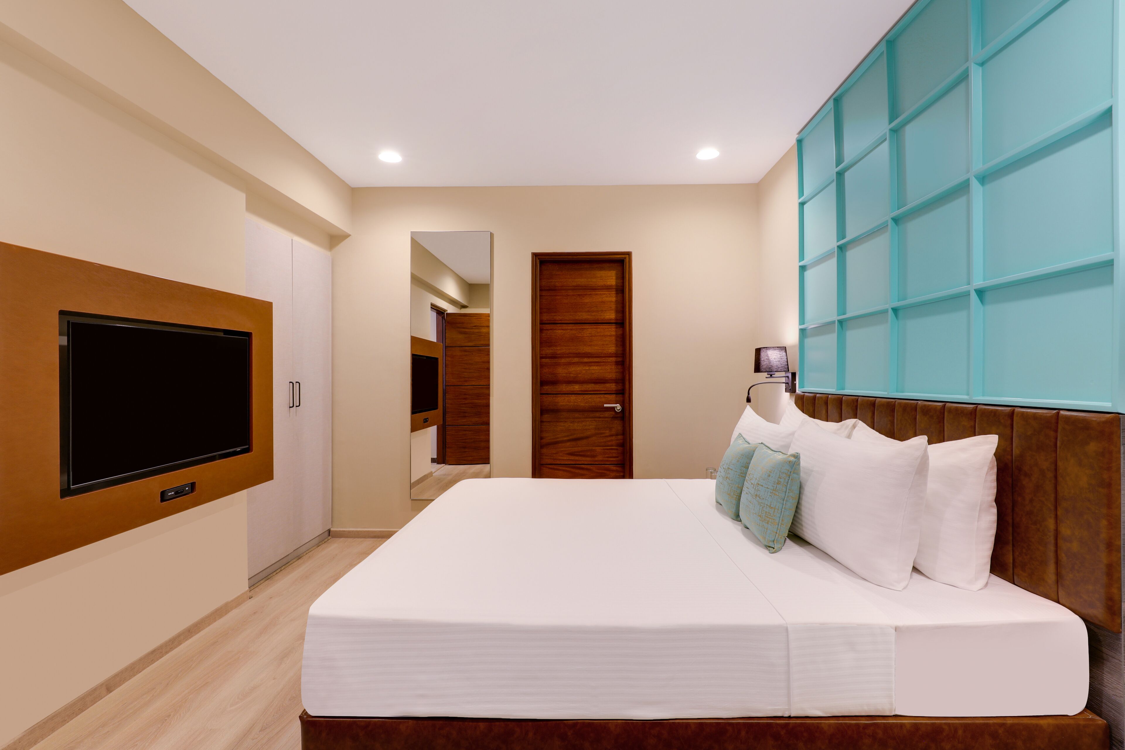 A bedroom with a large bed, a television mounted on the wall, and a wardrobe.