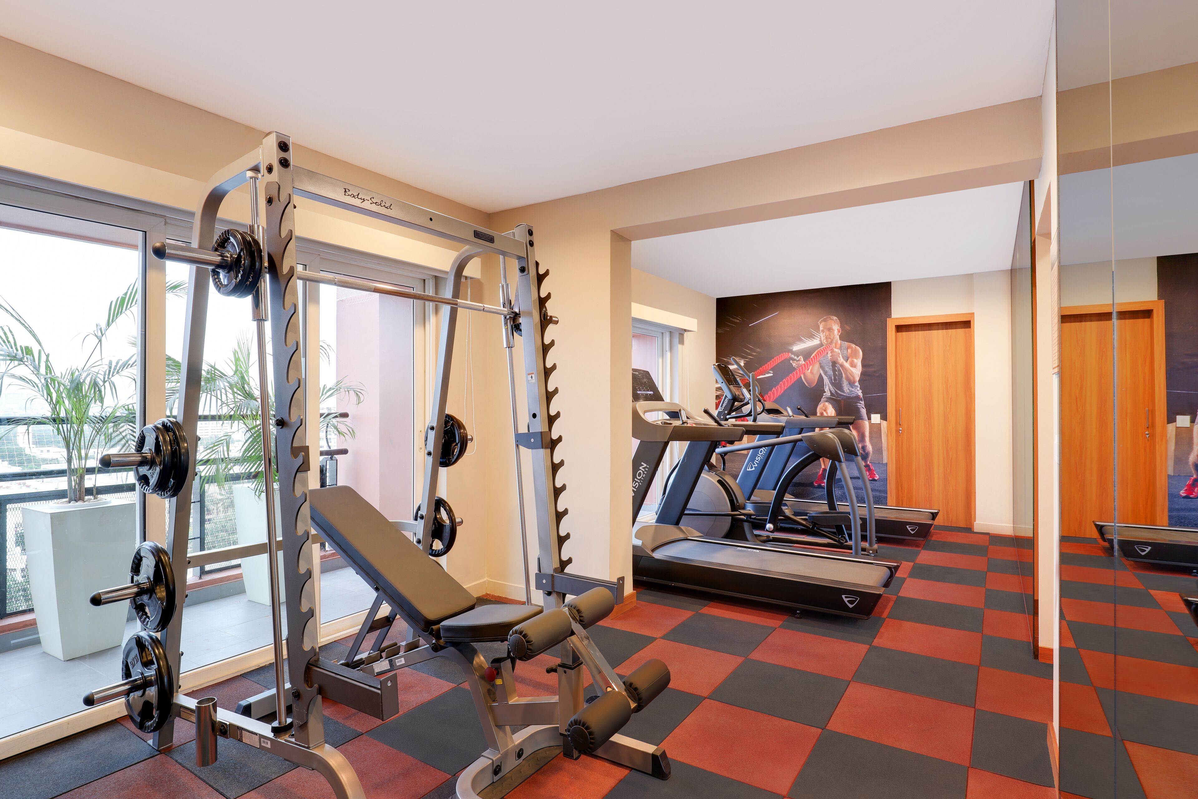 Un gimnasio con equipo de levantamiento de pesas, cintas de correr y un ventanal con vistas a palmeras.