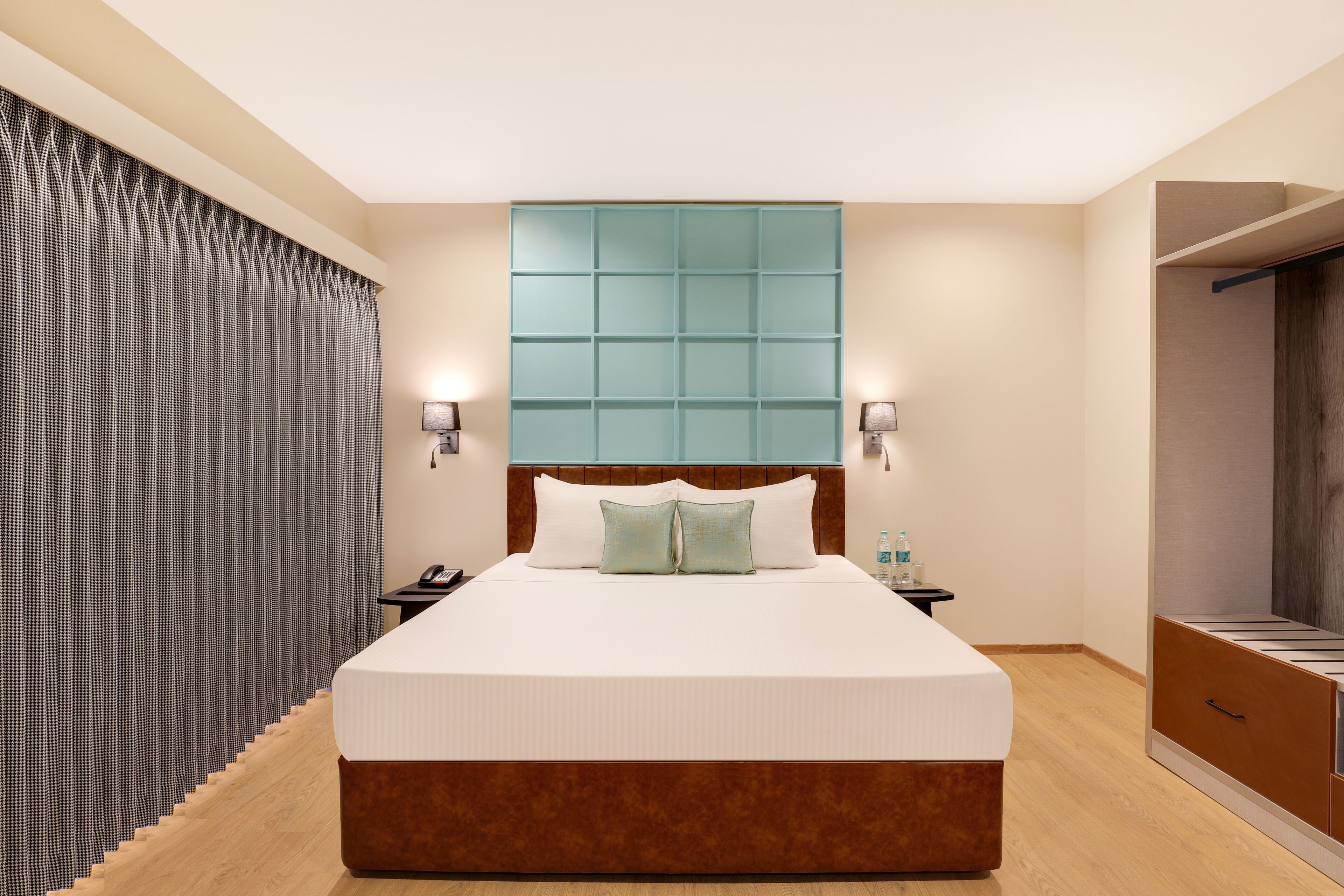 A hotel room with a large bed, a wooden headboard, a nightstand, a wall-mounted light, a curtain, and a closet.