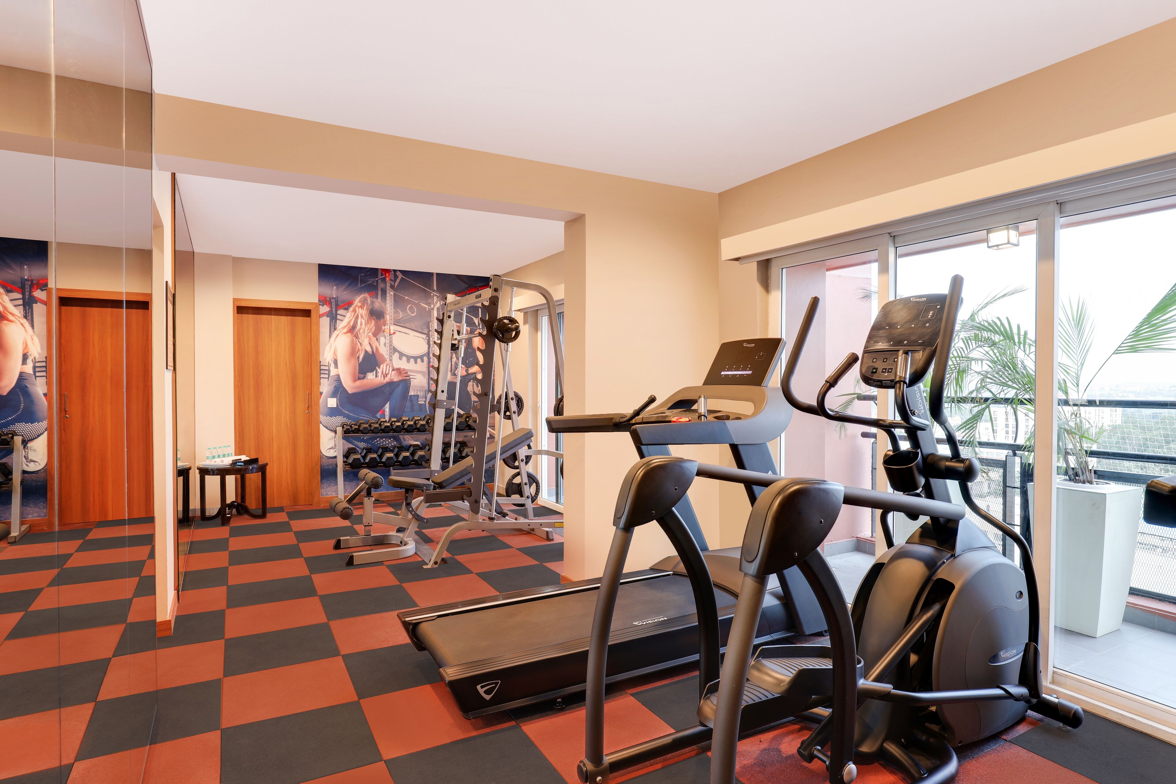 A gym with cardio machines, weight equipment, and a large window with a view of palm trees.