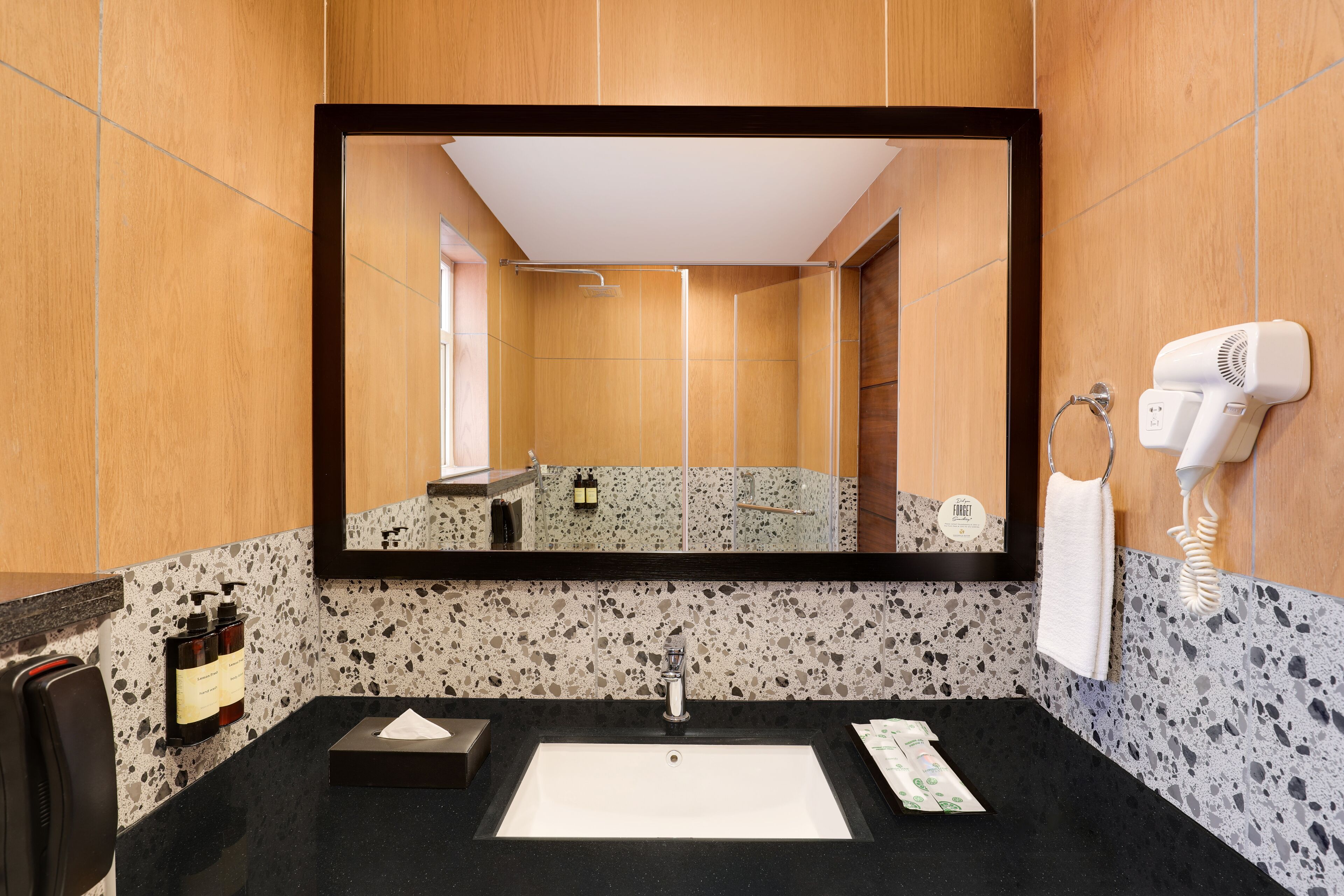 A bathroom with a black countertop, a white sink, a mirror, a hairdryer, and toiletries.