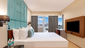 Ett hotellrum med en stor säng, en TV, ett skrivbord och utsikt över staden.