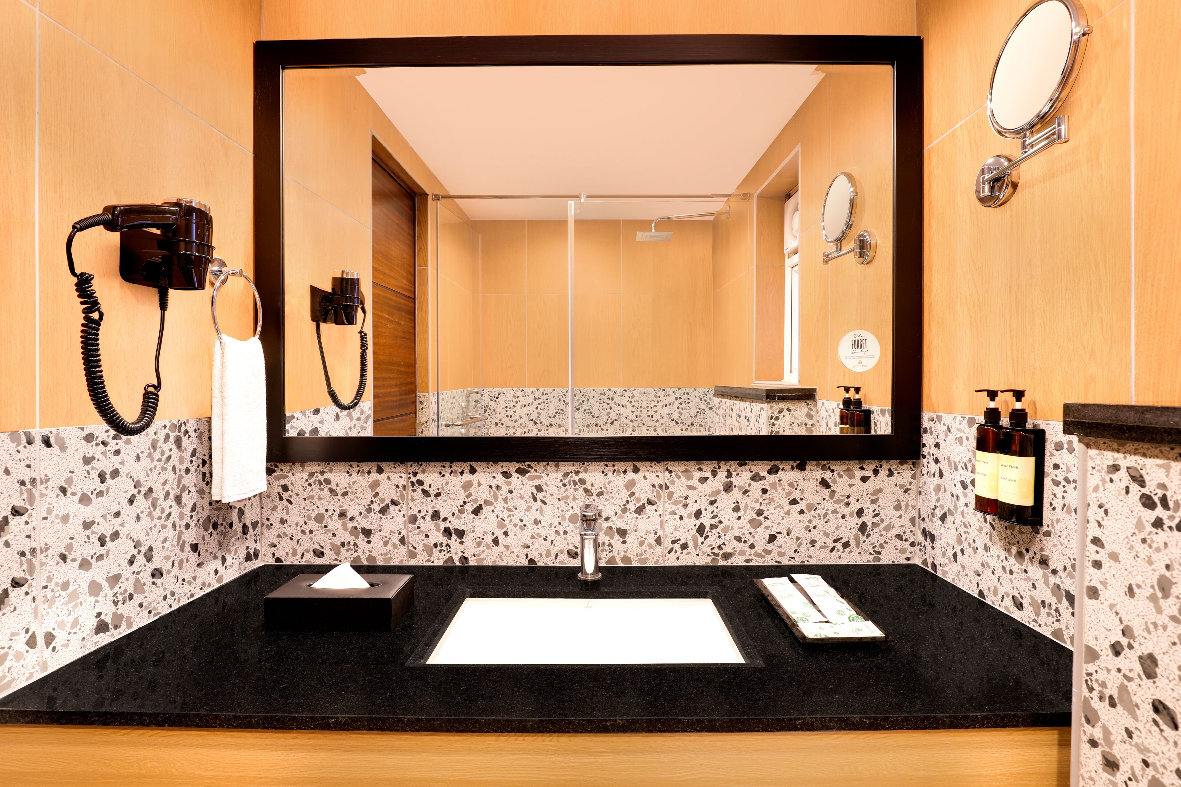 A bathroom with a black countertop, a sink, a mirror, a hairdryer, and toiletries.
