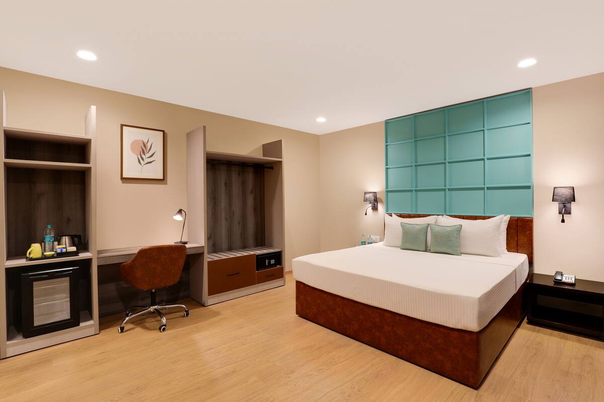 A hotel room with a large bed, a desk with a chair, a wardrobe, and a bathroom area.
