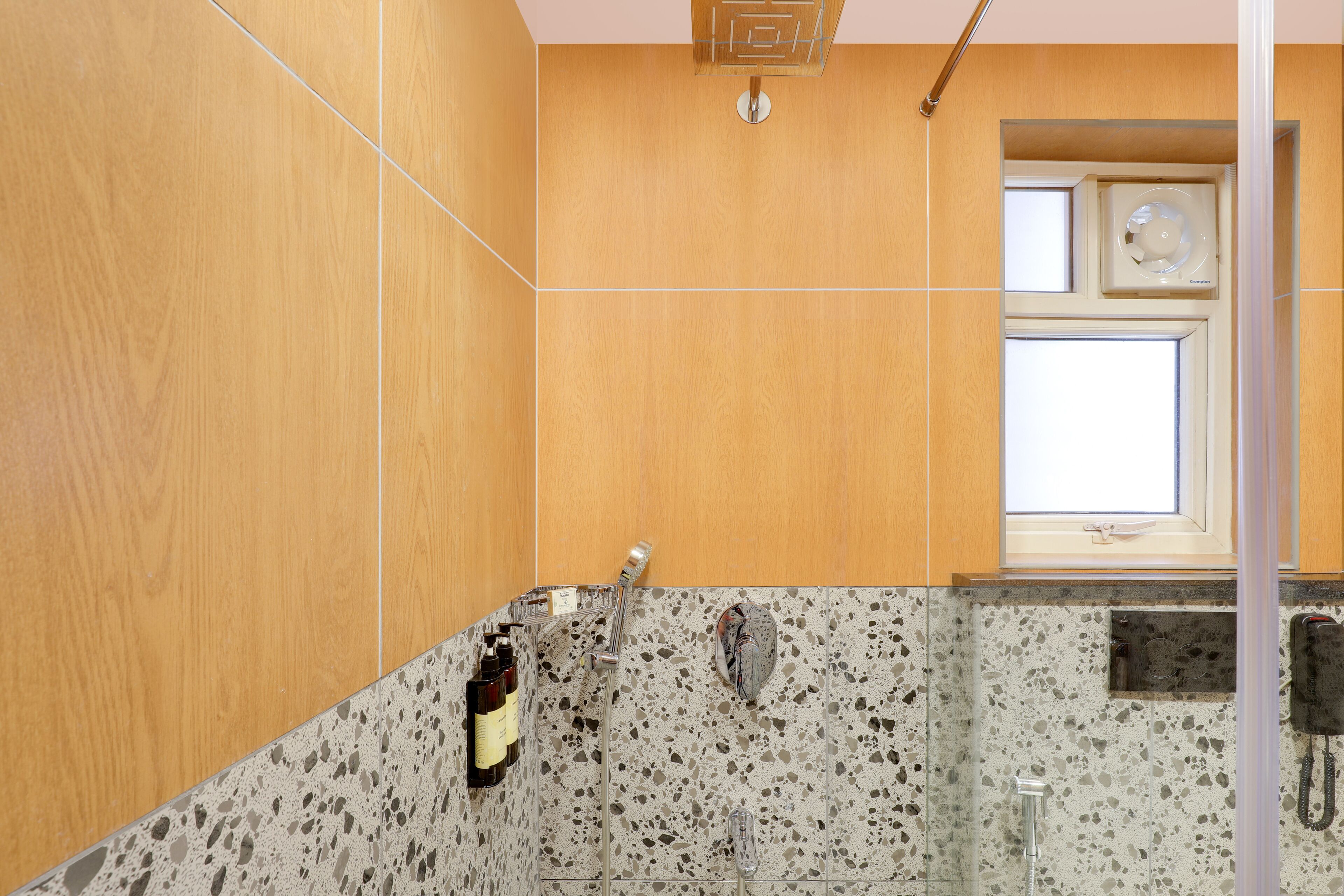 Un baño con tocador de madera, ducha con cabezal de ducha manual y ventana sobre el lavamanos.