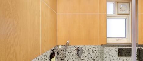Un baño con tocador de madera, ducha con cabezal de ducha manual y ventana sobre el lavamanos.