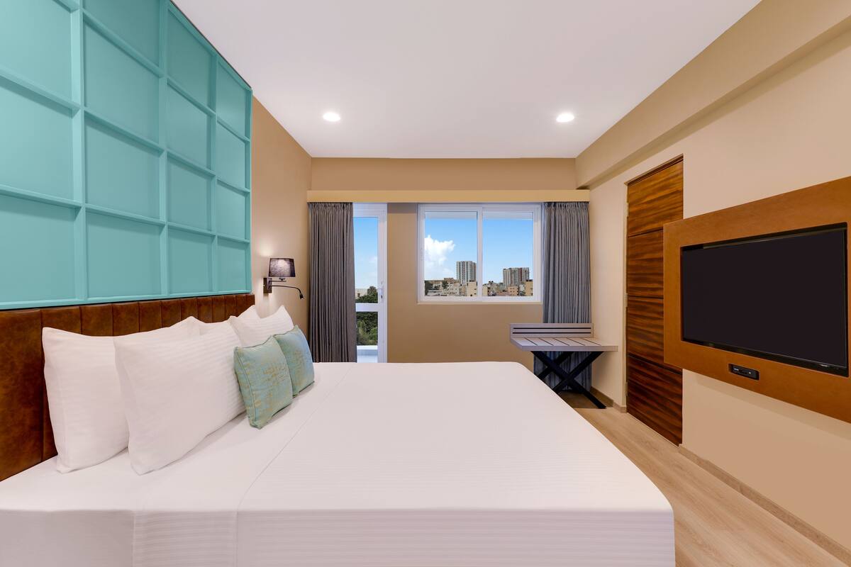 A hotel room with a large bed, a TV, a desk, and a view of the city.