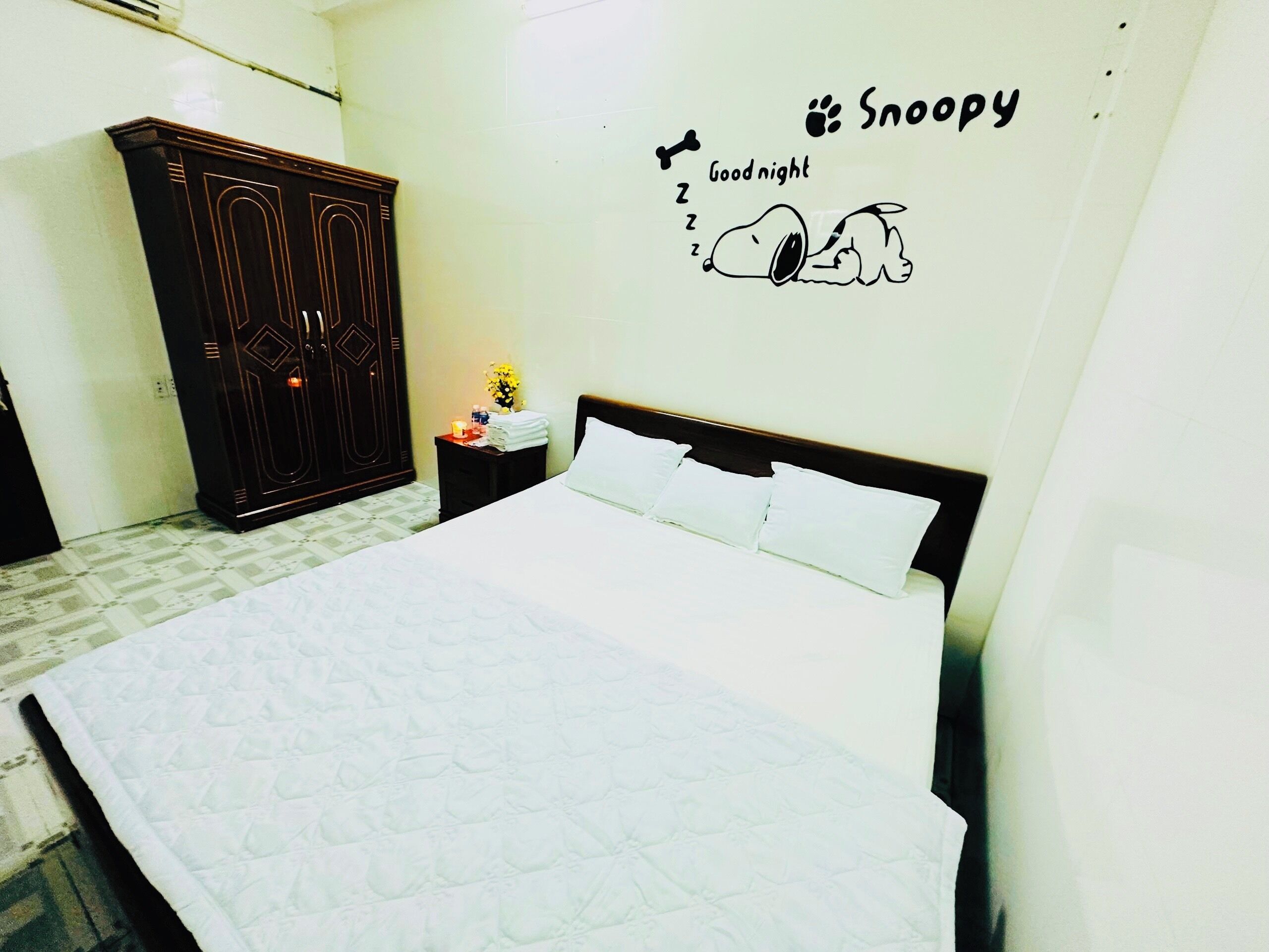 Une chambre avec un grand lit, une armoire et une décoration murale représentant Snoopy.