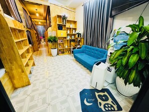 A cozy living area with a blue sofa, wooden shelves, and a potted plant. - The Dorm Tam Toà (Dong Hoi)