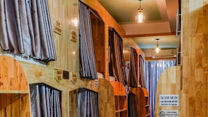 A row of wooden bunk beds with curtains, a patterned floor, and a sign indicating a smoking area. - The Dorm Tam Toà (Dong Hoi)