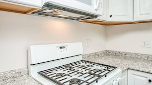 Une cuisine avec un fourneau blanc, un plan de travail en granit et des armoires blanches.