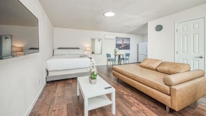 Une pièce moderne et bien éclairée, comprenant un lit, un canapé, une petite table avec un vase et un coin repas avec des chaises et une table.