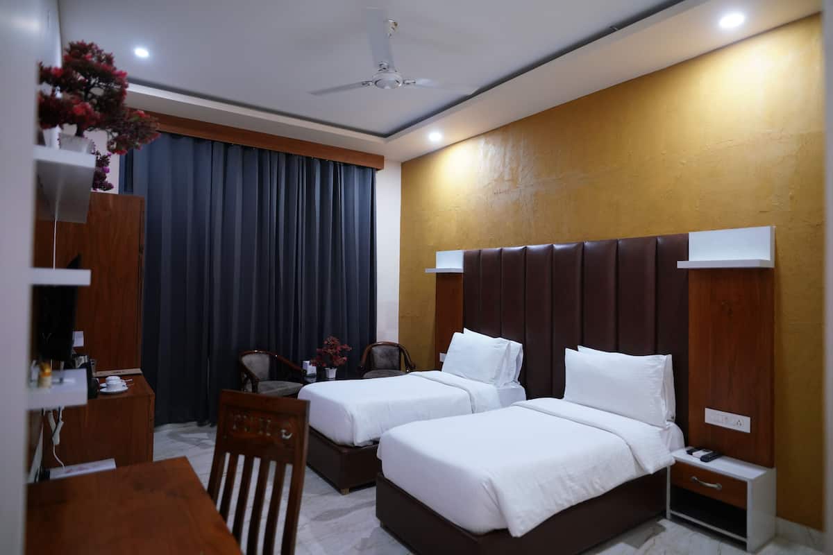 Quarto de hotel com duas camas, uma escrivaninha, uma cadeira, uma mesinha, uma mesa de cabeceira e um ventilador de teto.