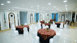 A banquet hall with round tables covered in red tablecloths, white chairs, and blue walls with arched doorways. - Golden Hut Derabassi (Dera Bassi)