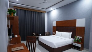 A hotel room with a large bed, a desk, a chair, a TV, and a nightstand with a vase of flowers. - Golden Hut Derabassi (Dera Bassi)