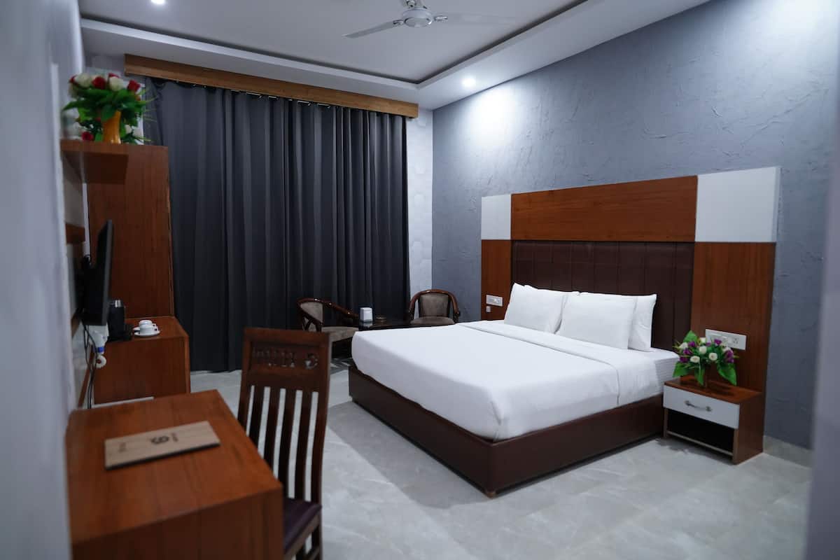 Quarto de hotel com uma cama grande, uma escrivaninha, uma cadeira, uma televisão e uma mesa de cabeceira com um vaso de flores.
