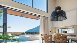 Een modern interieur met een groot raam, een hanglamp, een zwembad en rieten meubels.
