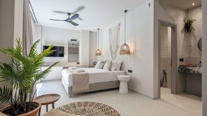 Een moderne slaapkamer met een bed, nachtkastjes, een plafondventilator en een badkamer met wastafel en douche.