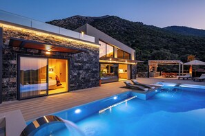 Eine moderne Villa mit Swimmingpool, Steinhausfassade und Blick auf eine gebirgige Landschaft.