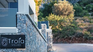 Ein Schild mit der Aufschrift 'Troia Villas', im Hintergrund eine Steinsäule und ein modernes Gebäude.