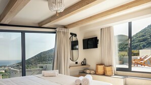 Ein Schlafzimmer mit einem großen Bett, einem an der Wand montierten Fernseher und Blick auf einen Balkon mit Gartenmöbeln.