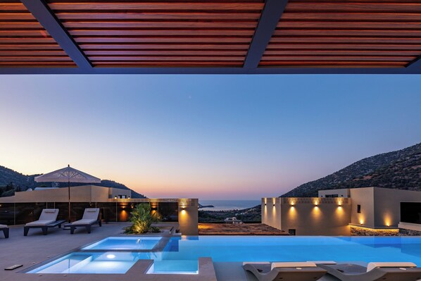 Ein moderner Poolbereich im Freien mit Liegestühlen und Blick auf das Meer im Abendlicht.