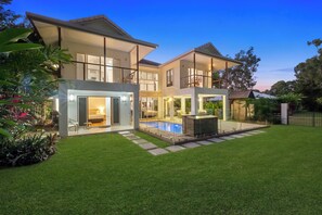 Una casa moderna de dos pisos con piscina, un patio cubierto y un césped bien cuidado.