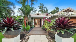 A house with a wooden pathway leading to the entrance, surrounded by tropical plants and trees. - This stunning home is located in Palm Cove. Short 5min walk to the beach. (Palm Cove)