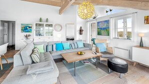 A modern living room with a grey sofa, wooden ceiling beams, a hanging light fixture, and a view of the outdoors through large windows. - "Elfi" - 700m from the sea by Interhome (Ringkøbing)