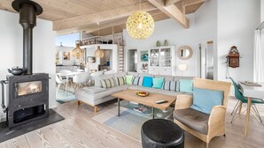 A modern living room with a wood-burning stove, a sofa set, a dining area, and a kitchen in the background. - "Elfi" - 700m from the sea by Interhome (Ringkøbing)