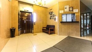 Zona de recepción con un banco, un bote de basura y un tablón informativo en la pared.